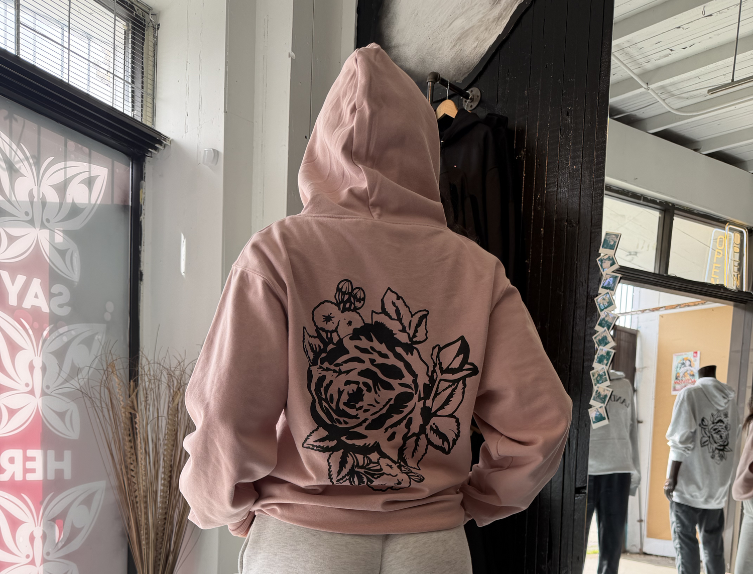 Person wearing a pink hoodie with a black floral design in an indoor setting.